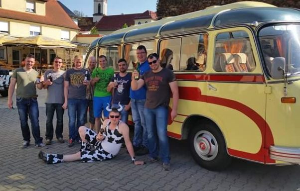 Gruppe von Personen lächelnd vor einem alten, gelben Reisebus im Freien.