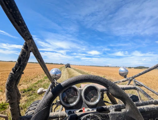 Blick von einem Buggy auf einen Feldweg unter blauem Himmel.