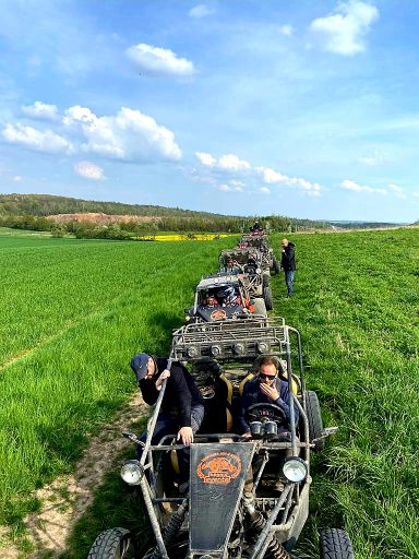 Mehrere Personen in Buggys fahren durch eine grüne Landschaft unter blauem Himmel.