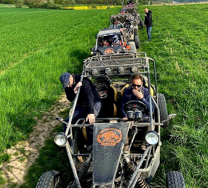 Eine Gruppe von Menschen fährt in Buggy-Fahrzeugen durch ein grünes Feld.