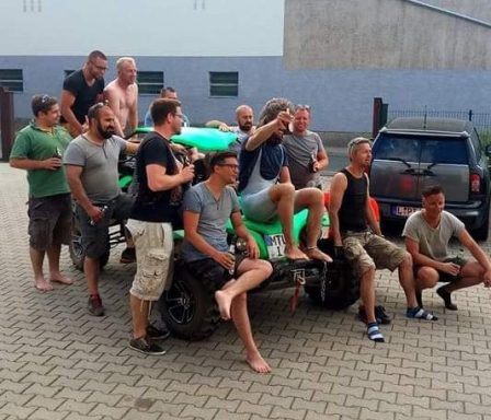 Eine Gruppe von Männern sitzt auf einem Quad in einem Hof. Sie lachen und unterhalten sich.