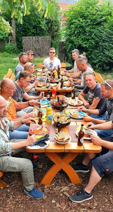 Feierliche Grillrunde mit mehrere Personen an einem langen Tisch im Freien.
