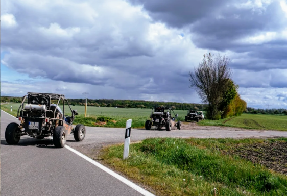 Vierte Offroad-Fahrzeuge fahren auf einer Landstraße in ländlicher Umgebung.