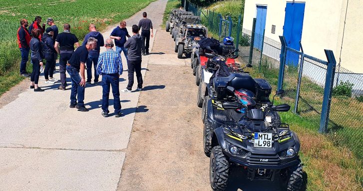 Gruppe von Personen neben einer Reihe von Quads auf einem Feldweg.