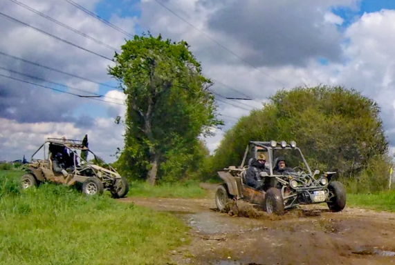 Zwei Offroad-Fahrzeuge fahren durch einen schlammigen Weg unter bewölktem Himmel.