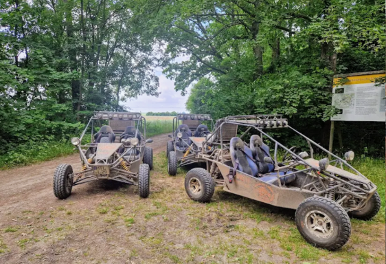 Zwei Offroad-Buggys stehen auf einem Schotterweg umgeben von Bäumen.